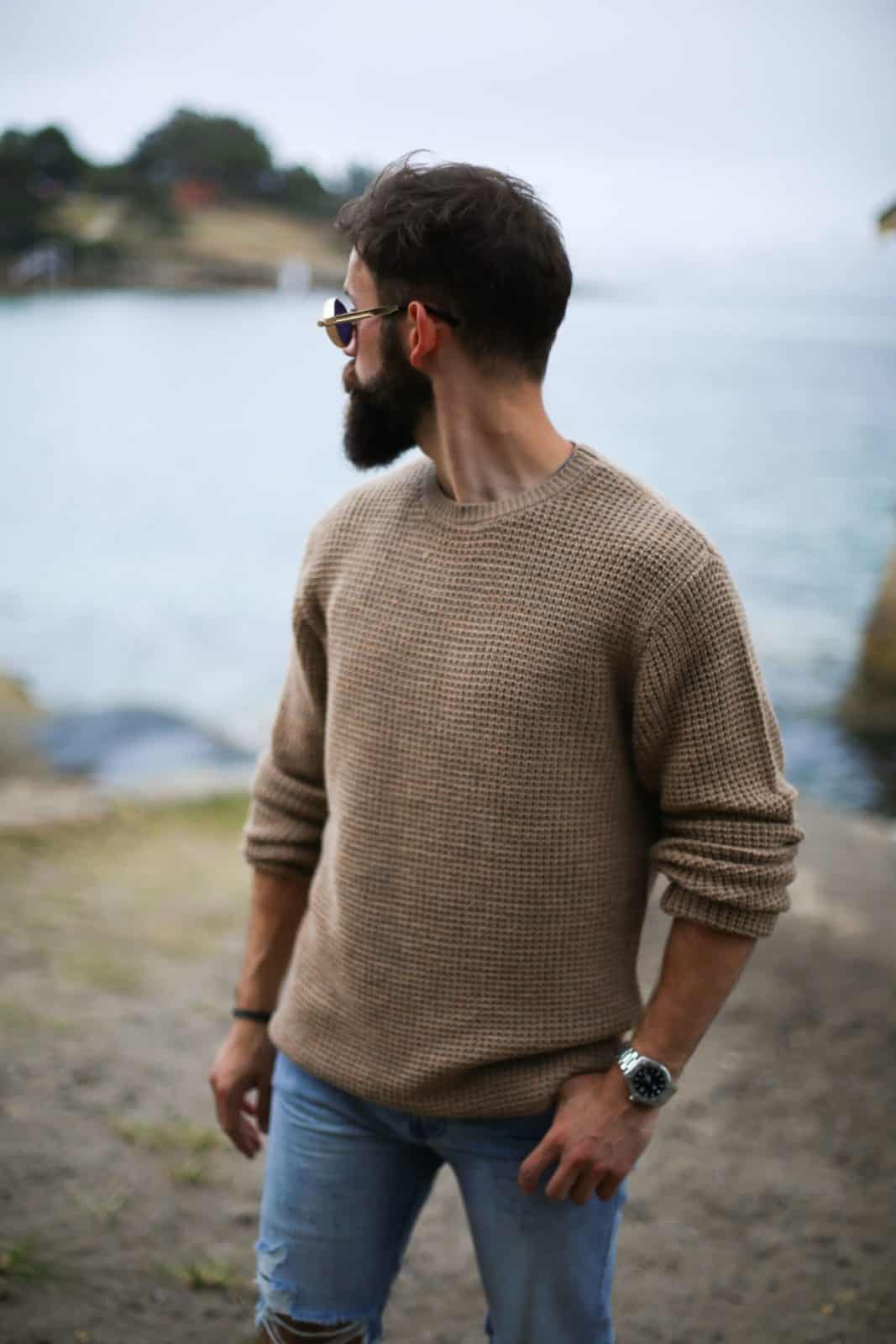 A man with a beard wearing a sweater and jeans.