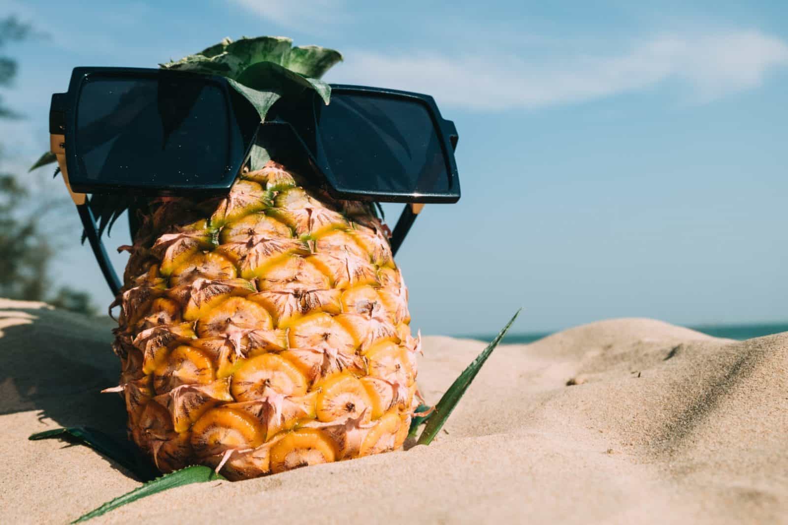 Sunglasses on a pineapple in the sand.