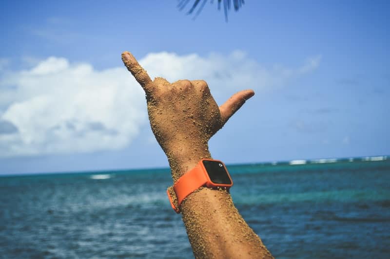 A person with an apple watch is making a hand gesture in front of the ocean.