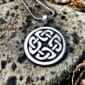 A silver celtic knot pendant on a rock.
