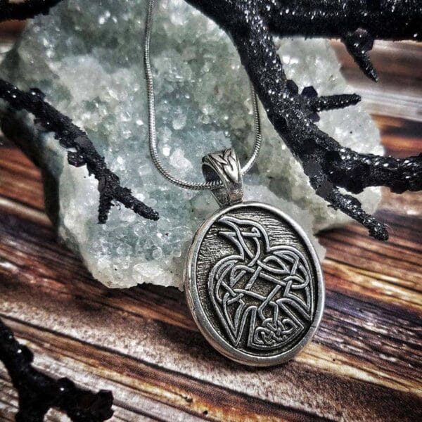 A silver pendant with an image of a raven on it.
