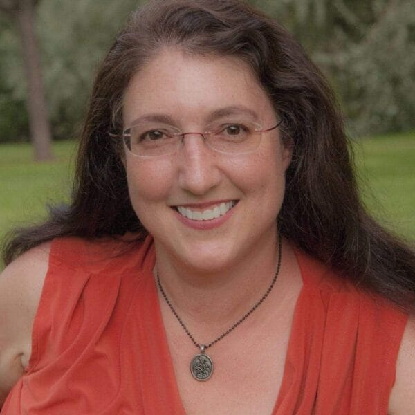 A woman in a red top is smiling in a field.