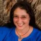 A woman wearing glasses and a blue shirt leaning against a tree.