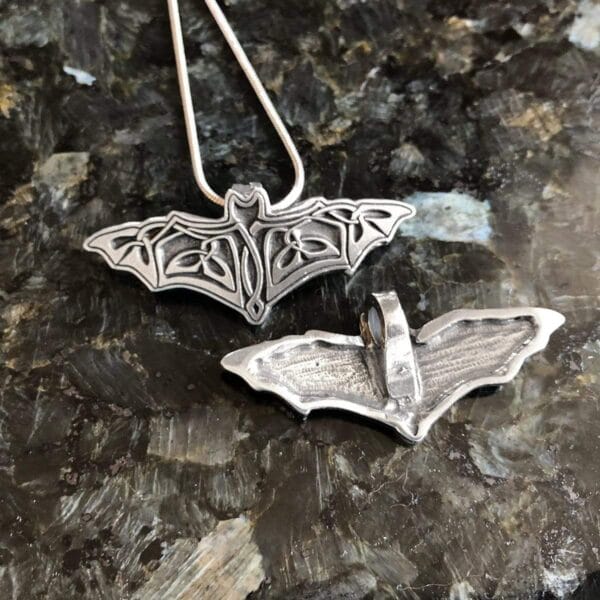 Two silver bat pendants on a table.