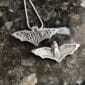 Two silver bat pendants on a table.