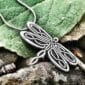 A dragonfly pendant is sitting on a leaf.
