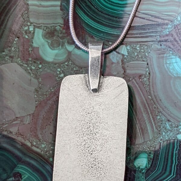 A silver dog tag necklace sitting on top of a marble.