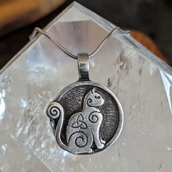 A silver cat pendant with a celtic design on it.