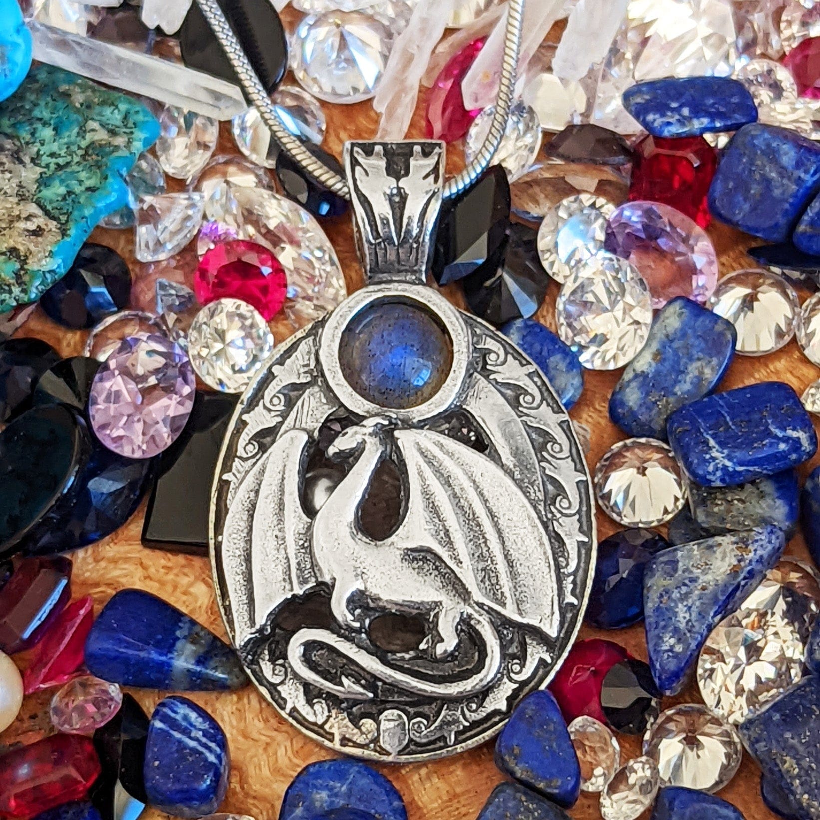 A pendant with a dragon on it surrounded by gemstones.