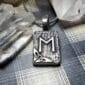 A silver pendant with the letter m on it.