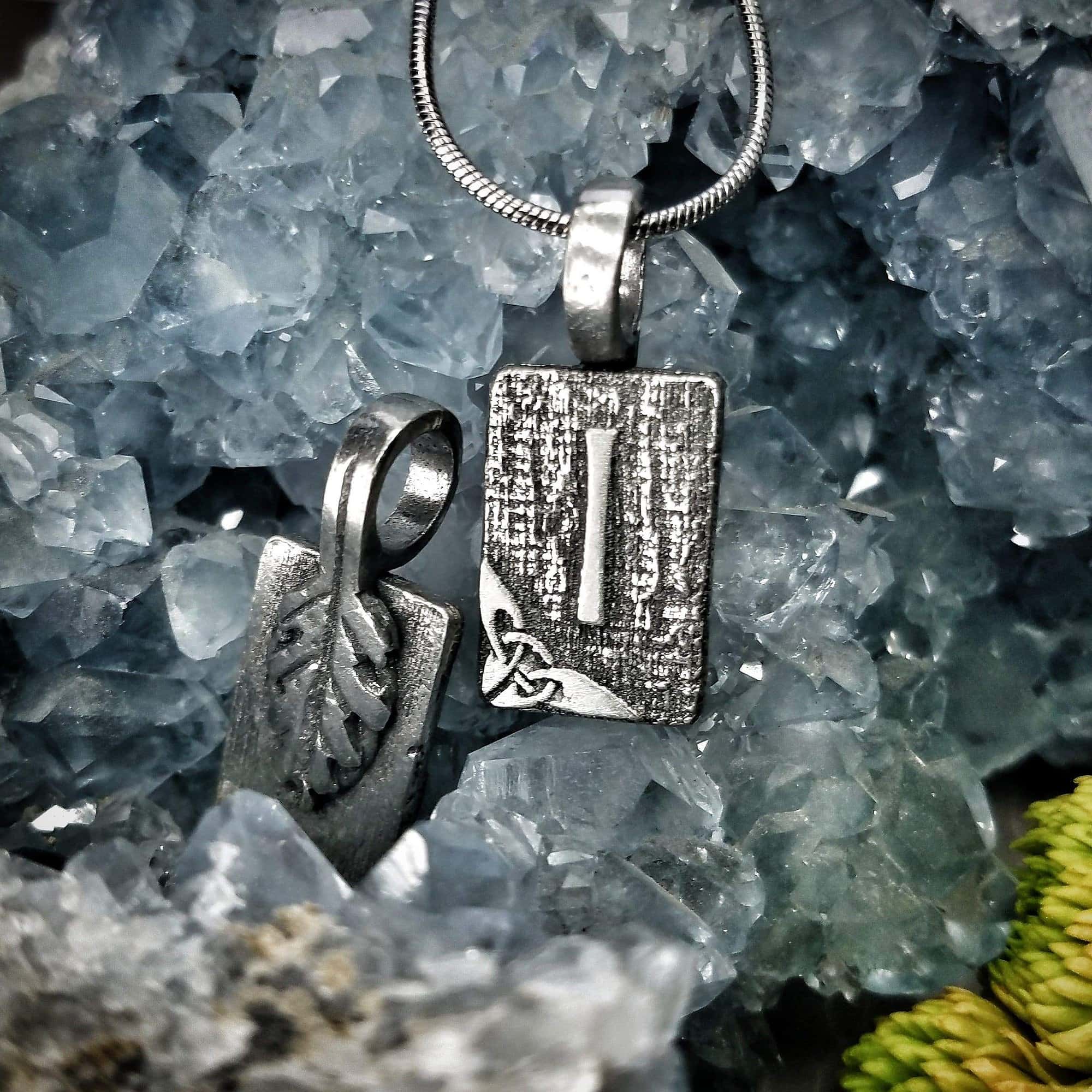 A silver pendant with a leaf on it.