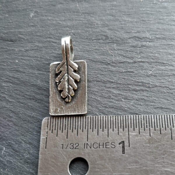 A small silver leaf charm on a ruler.