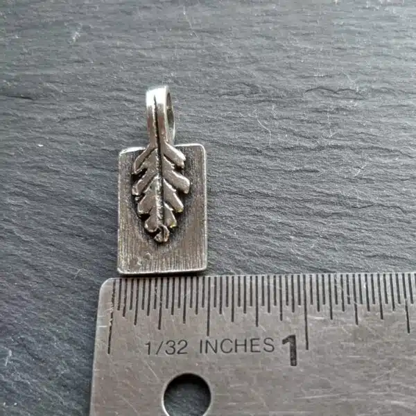 A small silver leaf charm on a ruler.