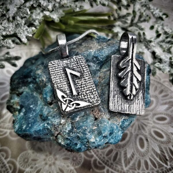 Two silver pendants with arrows and leaves on top of a rock.