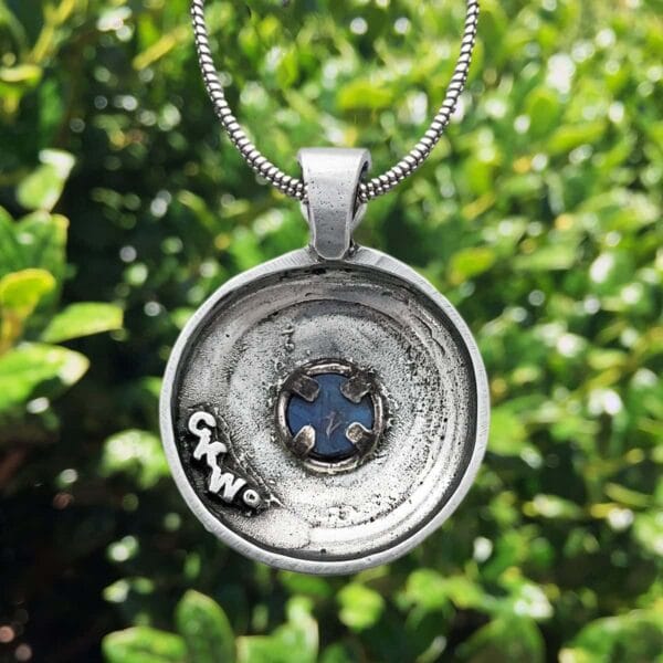 A silver pendant with a blue stone on it.