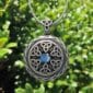 A silver celtic locket with a blue stone on it.