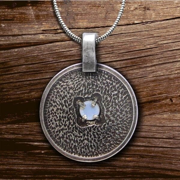 A silver pendant with a blue stone on it.