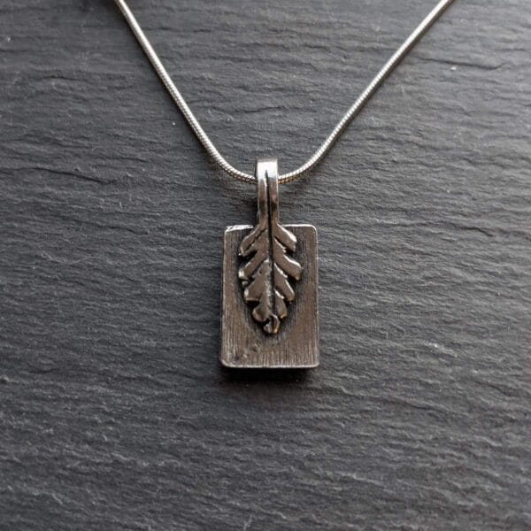 A silver pendant with a leaf on it.