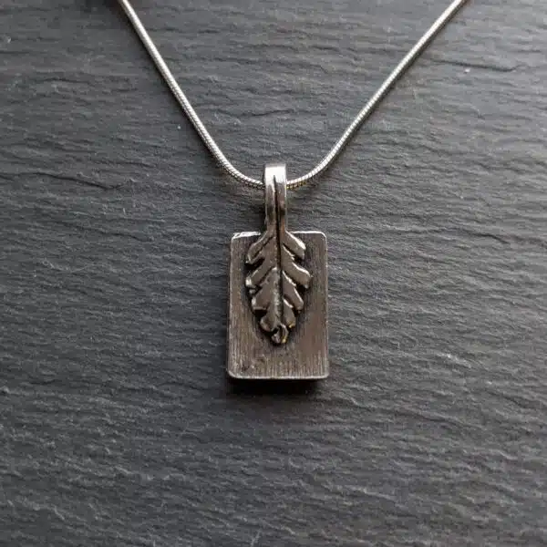 A silver pendant with a leaf on it. A silver pendant with a leaf on it.
