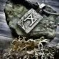 A silver pendant with the letter a on top of a rock.