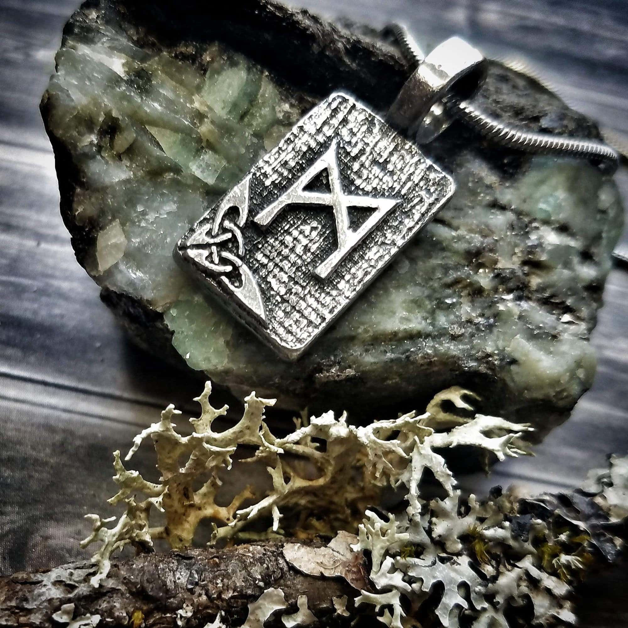 A silver pendant with the letter a on top of a rock.