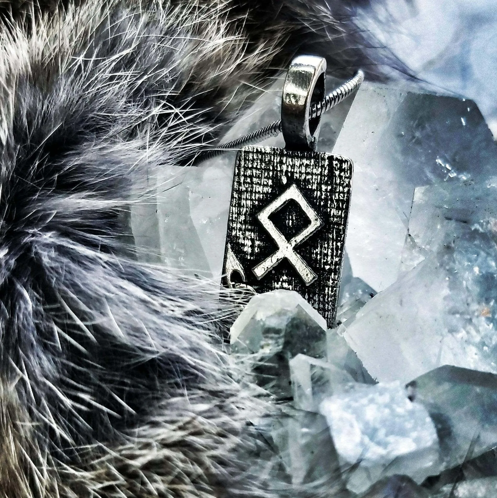 A silver pendant with a viking symbol on it.