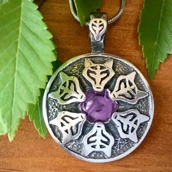 A silver pendant with a purple flower on it.