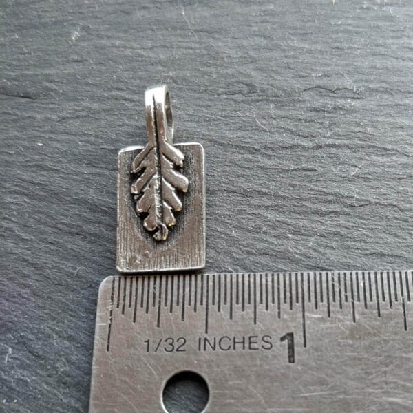 A small silver leaf charm on a ruler.