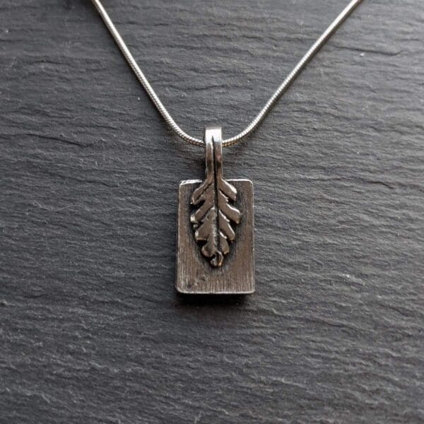 A silver pendant with a leaf on it.