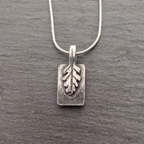 A silver pendant with a leaf on it.