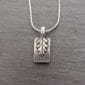 A silver pendant with a leaf on it.