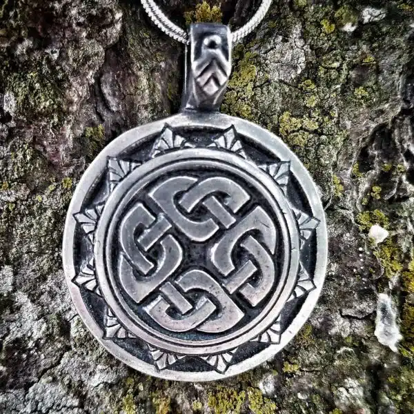 A silver pendant with a celtic design on it.
