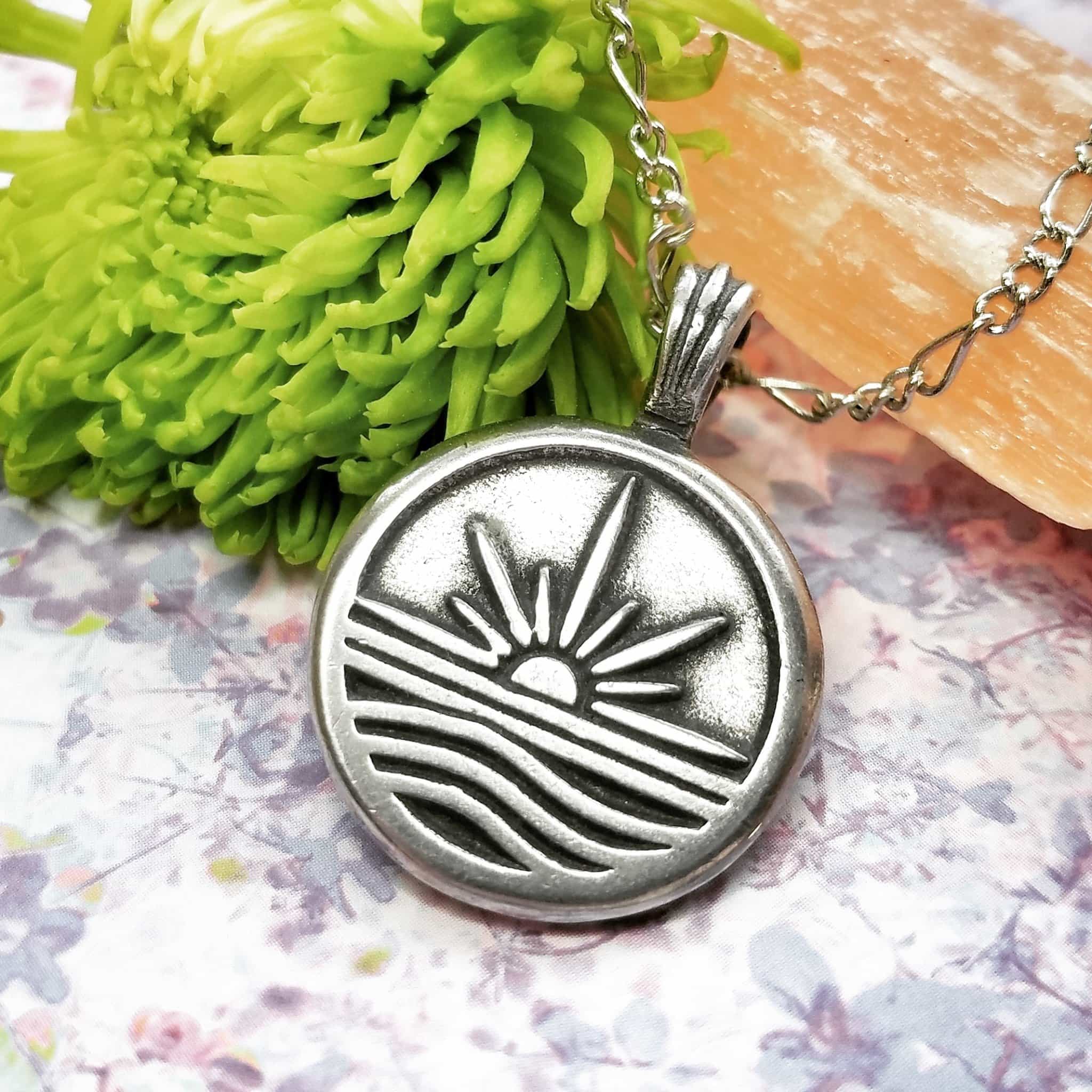 A silver pendant with a sun and waves on it.