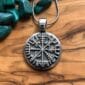 A silver pendant with a viking compass on it.