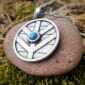 A silver pendant with a blue stone on top of moss.