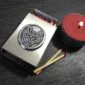 A matchbox with a red candle next to it.