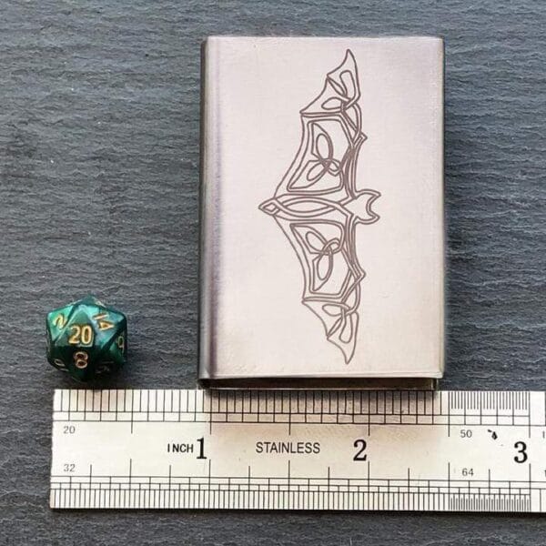 A metal case with a dice and a ruler next to it.