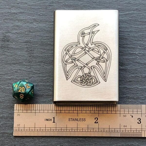 A metal case with a celtic design on it next to a ruler.