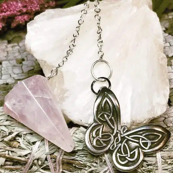 A silver pendant with a pink quartz and a butterfly on it.