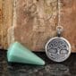 A celtic tree of life pendant and a silver cone on a rock.