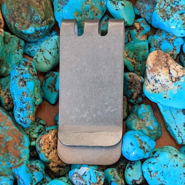 A silver money clip sitting on a pile of turquoise rocks.