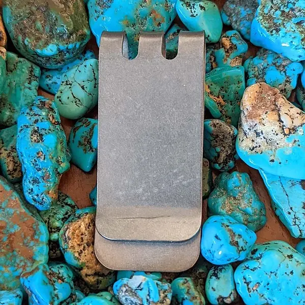 A silver money clip sitting on a pile of turquoise rocks.