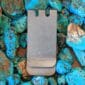 A silver money clip sitting on a pile of turquoise rocks.