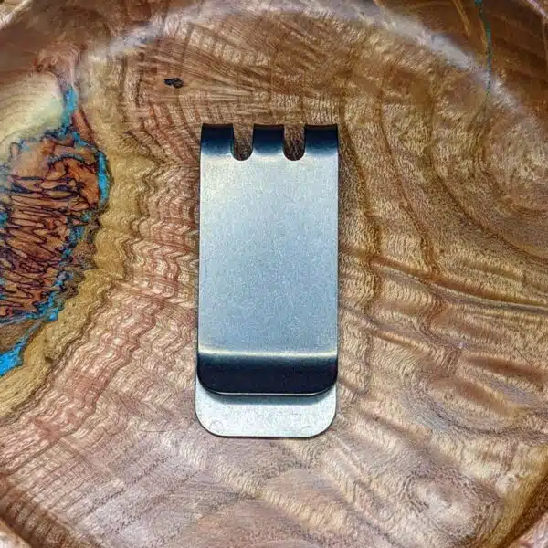 A metal money clip sitting on top of a wooden plate.