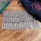 A Gather Rune Set 24pc Elder Futhark Pewter of viking symbols on a wooden table.