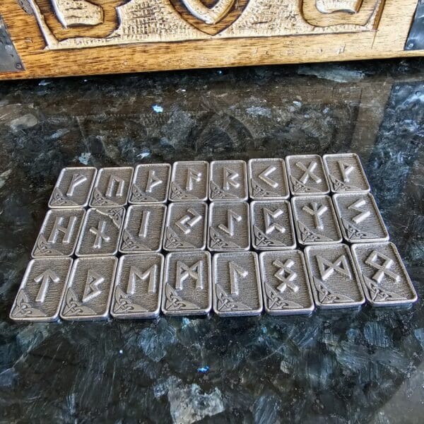 A Gather Rune Set 24pc Elder Futhark Pewter arranged on a table.