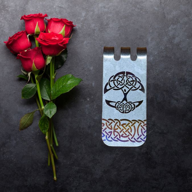 A bouquet of red roses lies next to a metal bookmark with Celtic knot designs on a dark surface.