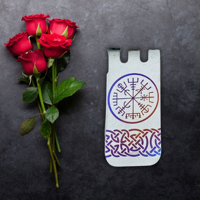 Red roses next to a phone case with a circular Norse design and a Celtic knot pattern on a dark surface.