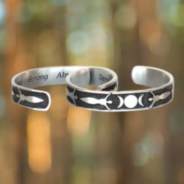 Triple Moon Bracelet The Triple Moon Bracelet set includes two silver metal cuffs with celestial designs of moons and stars, highlighted against a blurred forest backdrop.