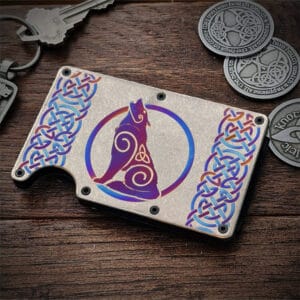 The Titanium Wolf Card Wallet, featuring a Celtic knot and stylized wolf design, sits on a wooden surface beside keys and Celtic themed coins.